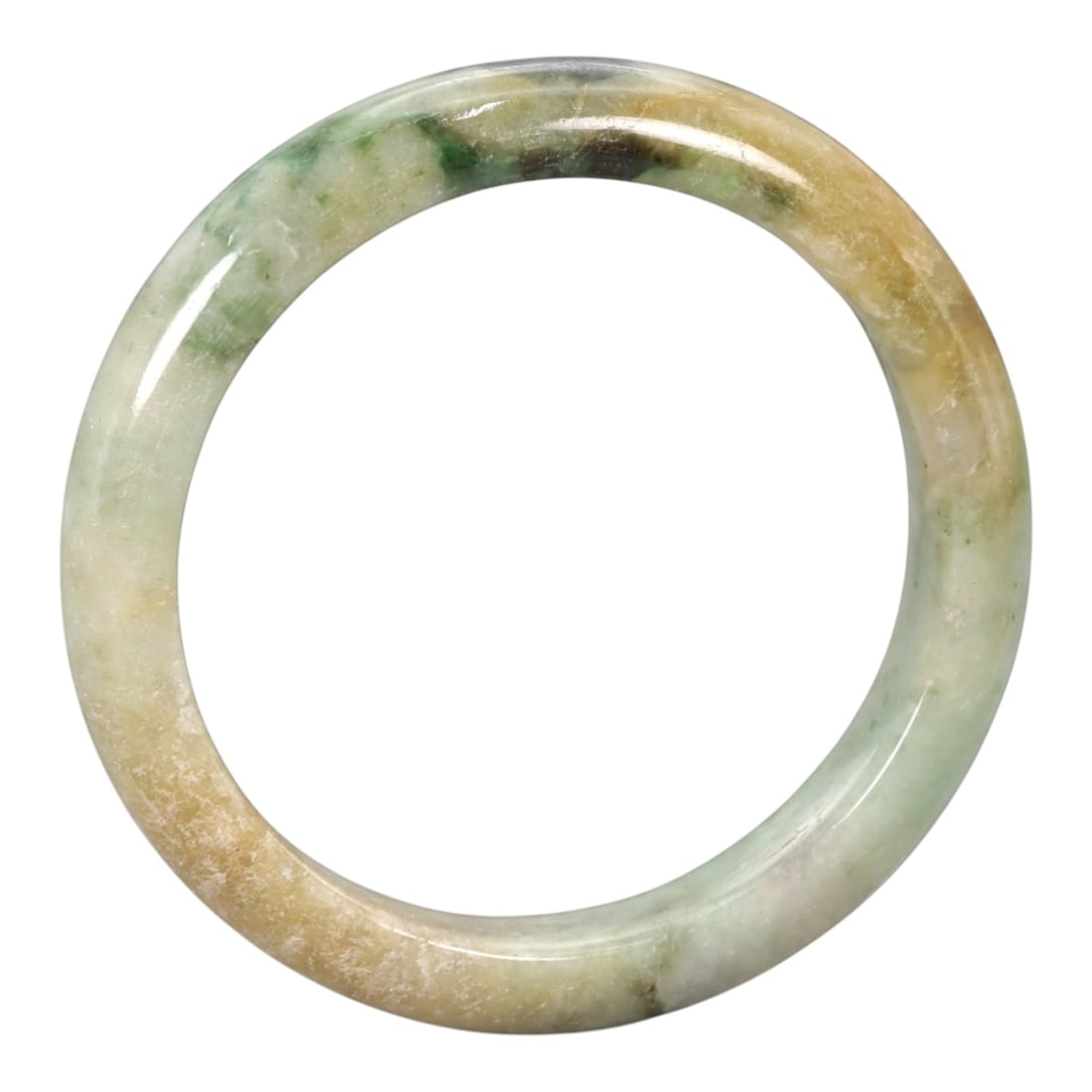 A Chinese Jadeite Jade Bangle Bracelet, 20th Century, 83ZK: Carved from jadeite jade with natural variegated coloration, including pale green, yellowish-brown, and darker green inclusions, the bangle is formed as a continuous circular band with a rounded, slig