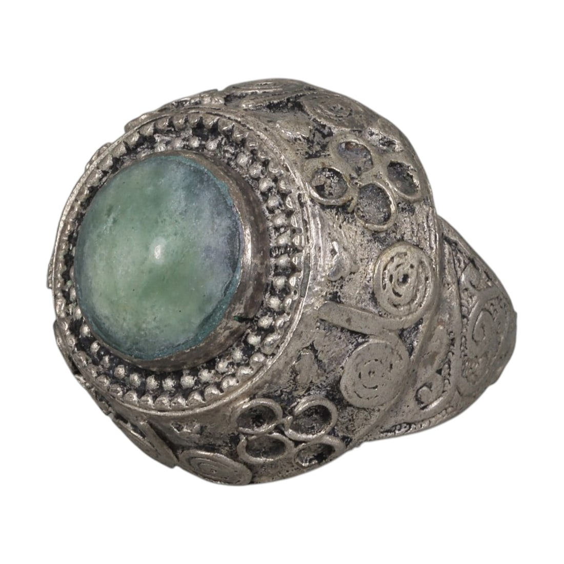A Middle Eastern Silver Plated Green Agate Ring, Late 19th-Early 20th Century, 23AK: The ring is centered with a round cabochon green agate stone exhibiting natural mottled green tones, set within a domed bezel framed by beaded granulation. The bezel and shoulders are decorated with a