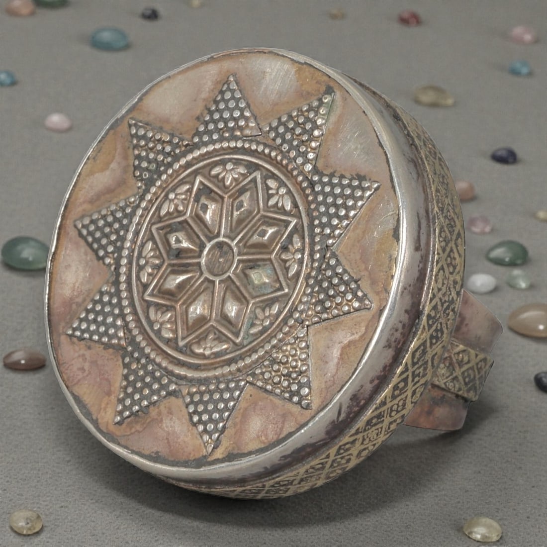 A Central Asian Silver Plated Geometric Star Motif Ring, Late 19th-Early 20th Century, 12AK: Crafted from silver plated metal with brass accents, featuring a wide, open band. The circular bezel displays a multi-layered star motif: a central eight-pointed star surrounded by small floral detail