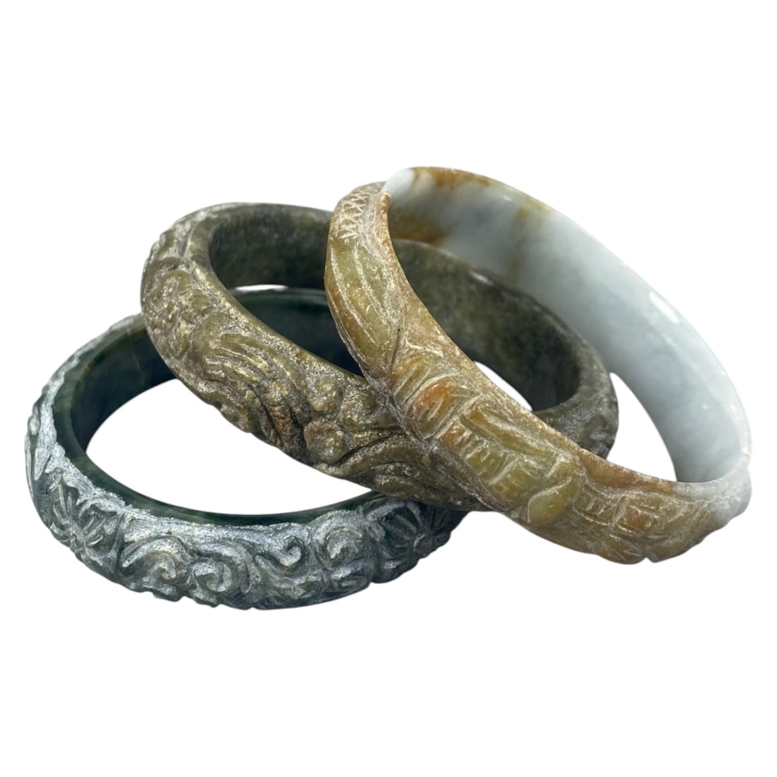 Lot of 3 Chinese Carved Jadeite Jade Bracelets (Bangles), 81AC: Each bracelet is carved from jadeite with varied natural coloration and patina, including deep green, weathered brownish-green, and pale grey-white with russet inclusions. The outer surfaces are adorn