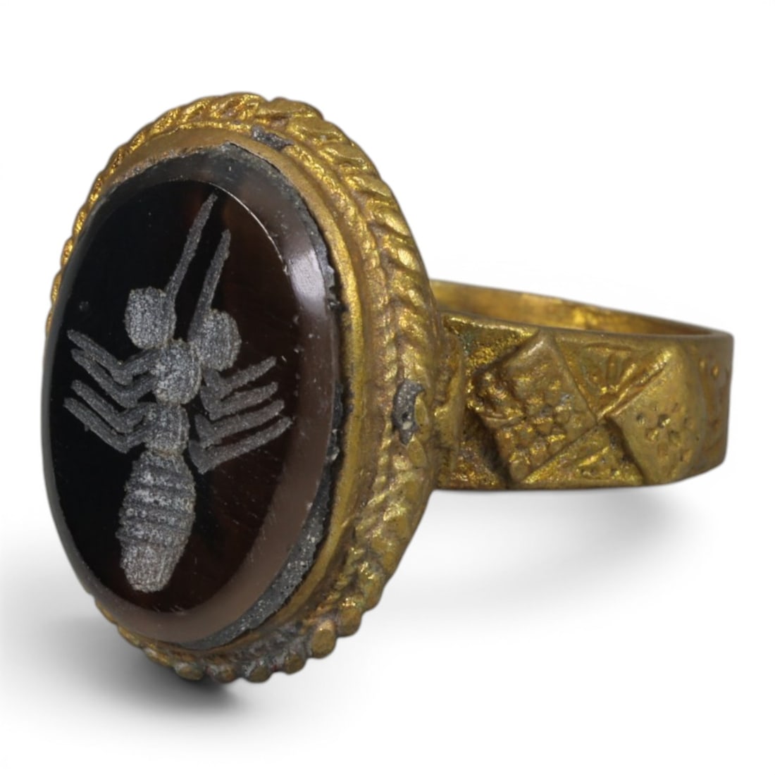 Antique Qajar Dynasty Gilt Intaglio Ring, US Size 9.5, 47AJ: A gilt-metal ring of the Qajar period, US ring size 9.5, featuring an oval dark stone (likely banded agate or similar) intaglio engraved with an ant motif. The bezel is decorated with a twisted rope-s