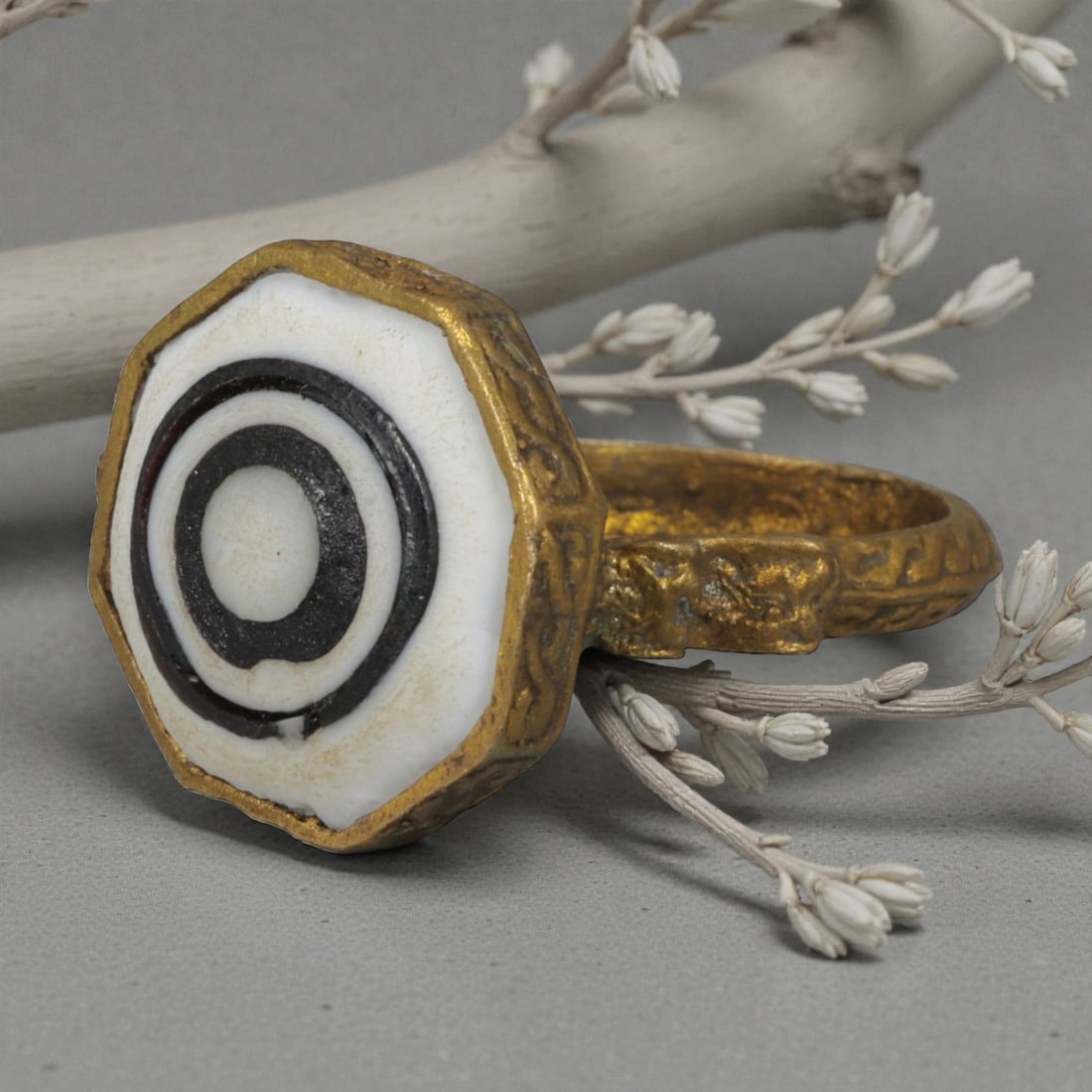 Antique Qajar Dynasty Gilt Evil Eye Ring, US Size 9, 9AJ: A gilt-metal ring of the Qajar period, US ring size 9, featuring an octagonal evil-eye glass inlay with a bold concentric black-and-white design. The bezel and band are adorned with detailed repousse 