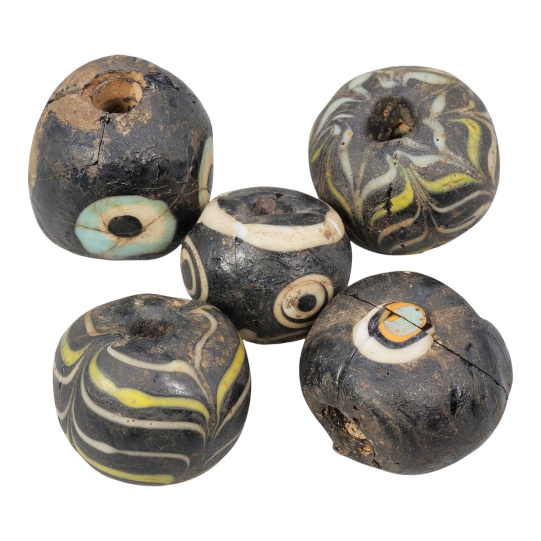 Lot of 5 Antique Islamic Glass Beads, Circa 9th-14th Century, 73AD: Comprising five beads ranging from 1.5 cm (5/8 in.) to 2 cm (3/4 in.), each formed from dark base glass with varied decorative motifs. Two beads feature feather-patterned trails in white, yellow, and 