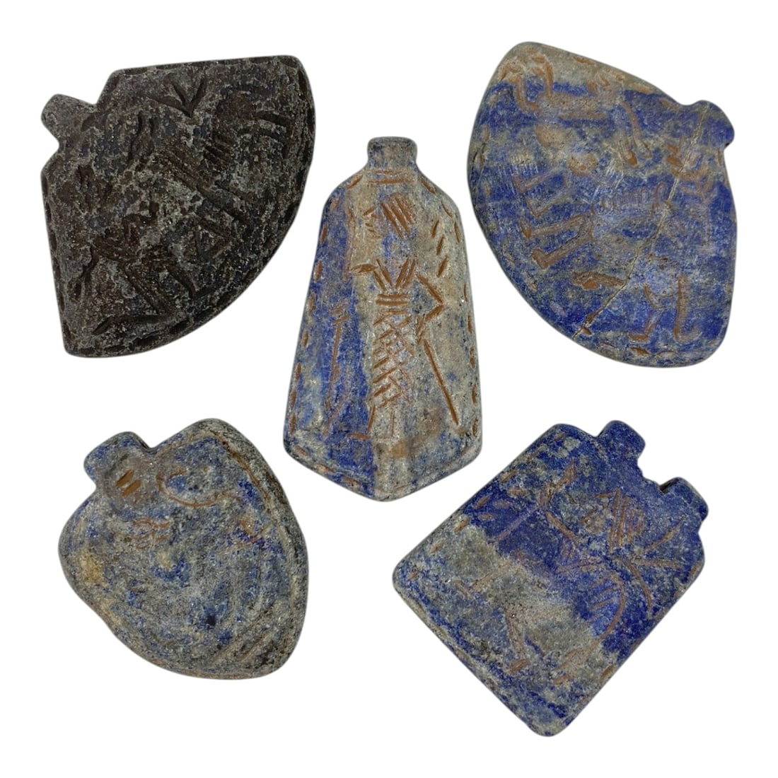 A Lot of 5 Ancient Near Eastern Lapis Lazuli Amulets, 11AC: The group comprises five amulets carved from lapis lazuli, with tones ranging from deep blue to weathered grey-blue, interspersed with natural mineral inclusions and surface patina consistent with ant