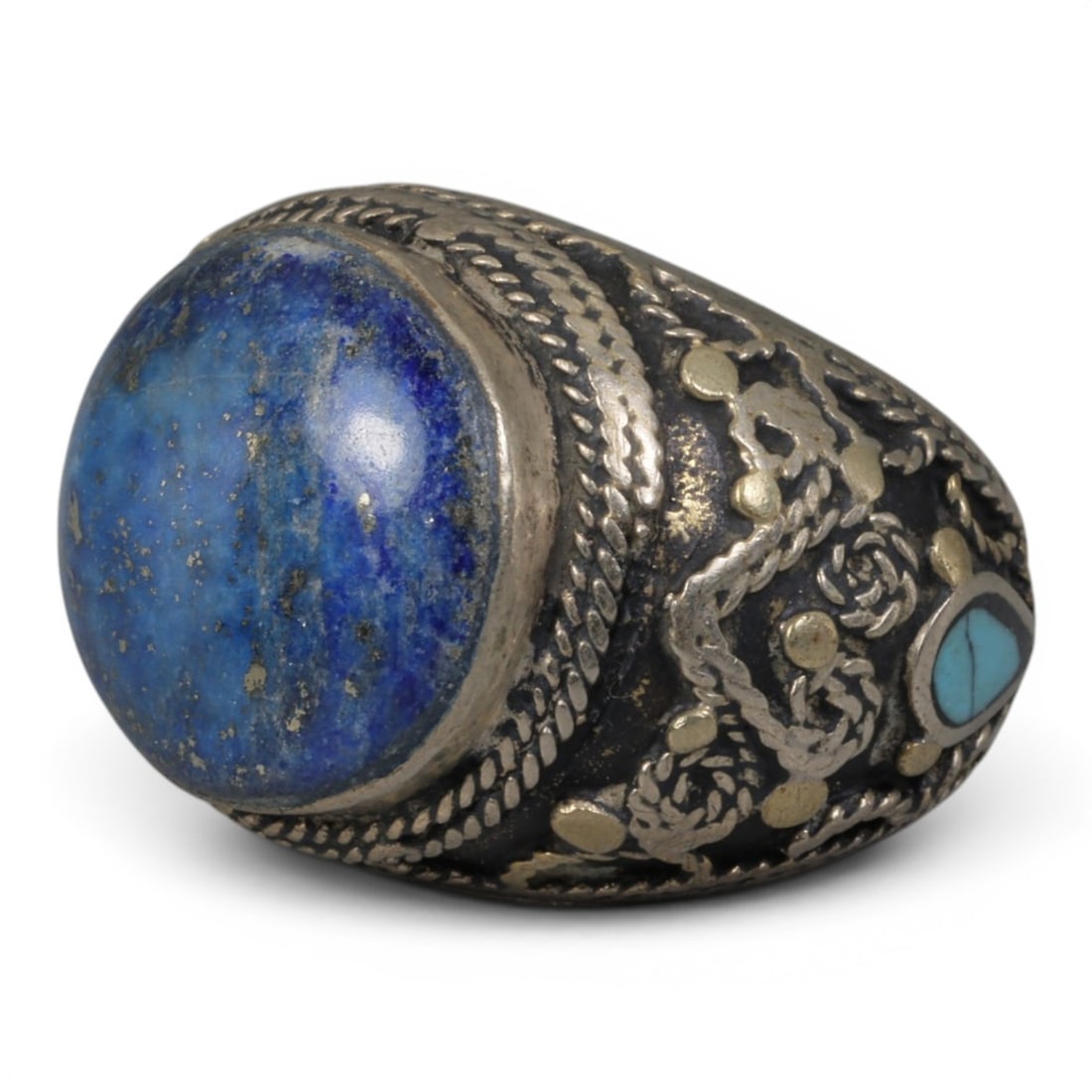 Antique Central Asian Silver and Lapis Lazuli Tribal Ring, 19th-Early 20th Century, 62AJ: The ring is set with a large, smooth cabochon lapis lazuli stone, displaying characteristic pyrite inclusions within its deep blue matrix. The silver mount is decorated with pseudo-filigree wirework, 