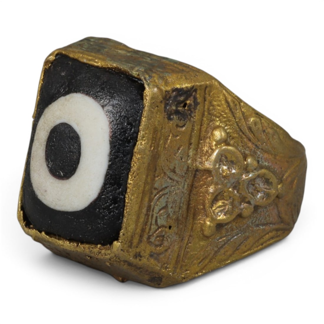 Antique Qajar Dynasty Gilt Evil Eye Ring, US Size 10, 25AJ: A gilt-metal ring of the Qajar period, US ring size 10, featuring a square evil-eye glass inlay with a bold concentric black-and-white design. The bezel and band are adorned with detailed repousse flo