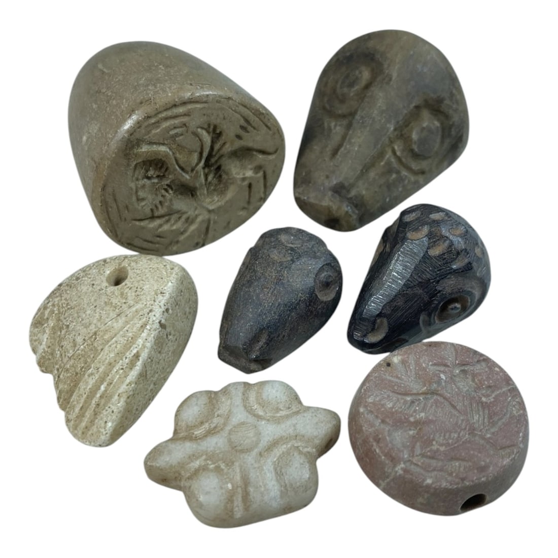 Lot of 7 Ancient Near Eastern Stone Amulets and Seals, 6AC: The group comprises seven carved stone objects, including zoomorphic head amulets, a floral-form pendant, and conical/button seals. Crafted from light and dark grey stone, off-white calcareous stone, 