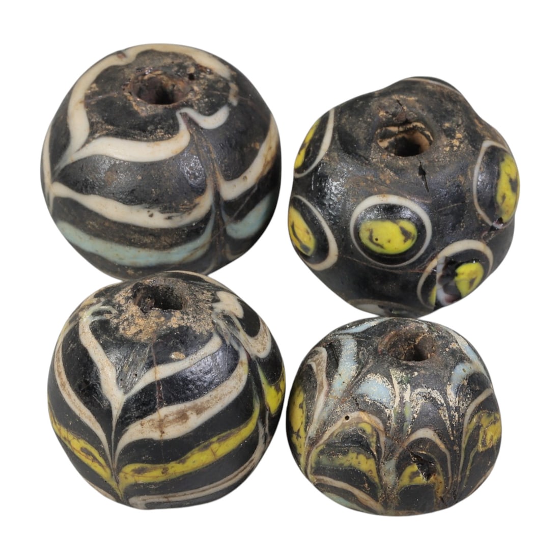 Lot of 4 Antique Islamic Feather-Patterned Glass Beads, Circa 9th-14th Century, 40WM: A group of four spherical glass beads, each with a central perforation. The beads display varied decorative techniques, including feather-patterned trailed glass and eye motifs, set against dark bases