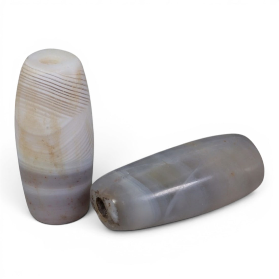 A Pair of Antique Central Asian / Himalayan Banded Agate Trade Beads, 15th-19th Century, 84AJ: The pair consists of two elongated, barrel-shaped banded agate beads. The standing bead displays fine, parallel grey and white striations with subtle reddish mineral inclusions, while the lying bead f