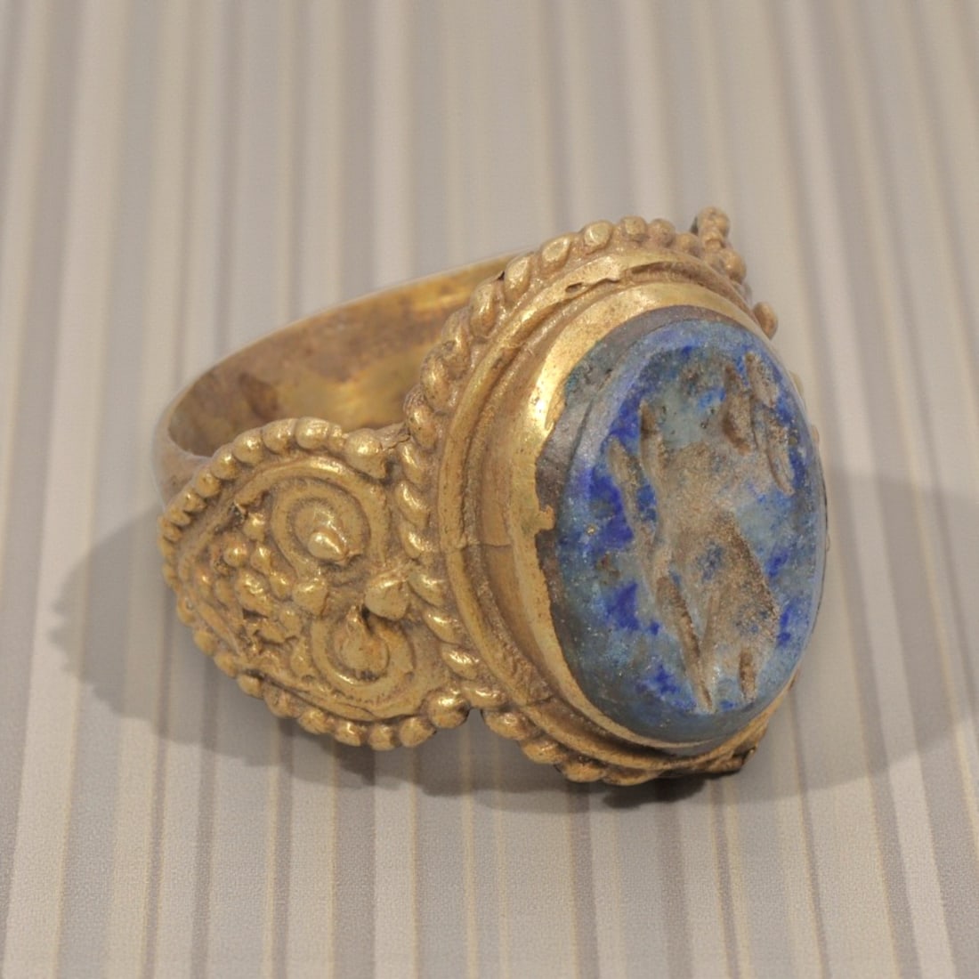 Antique Qajar Dynasty Gilt Intaglio Ring, US Size 9.5, 37WS: This ring features an oval lapis lazuli intaglio carved with a stylized motif, executed in the glyptic style characteristic of Qajar period Iran. The rich blue lapis displays natural mineral inclusion