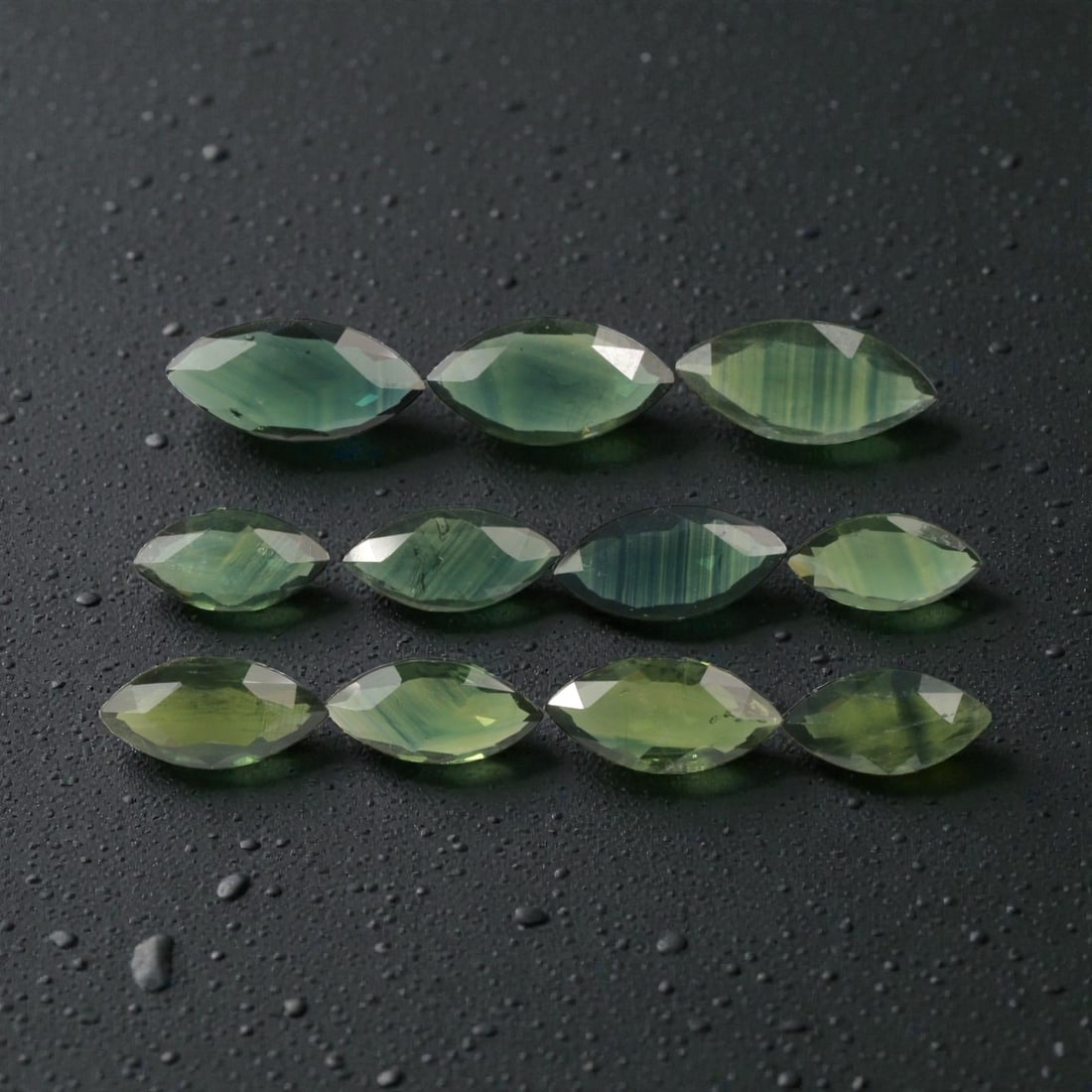 9.26 Carats Natural Banded Green Australian Sapphire Parcel - 11pcs Heated Only, 22YE: This parcel of 11 marquise-cut sapphires showcases a striking range of green hues, from soft yellow-green to deep teal, with prominent natural color banding visible across every stone. The elongated m