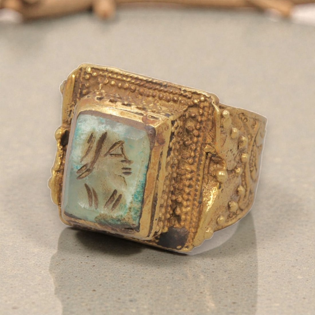 Antique Qajar Dynasty Gilt Intaglio Ring, US Size 10, 83WS: This ring features a rectangular turquoise-hued stone intaglio carved with a profile bust, executed in the glyptic style characteristic of Qajar period Iran. The stone displays natural color variation