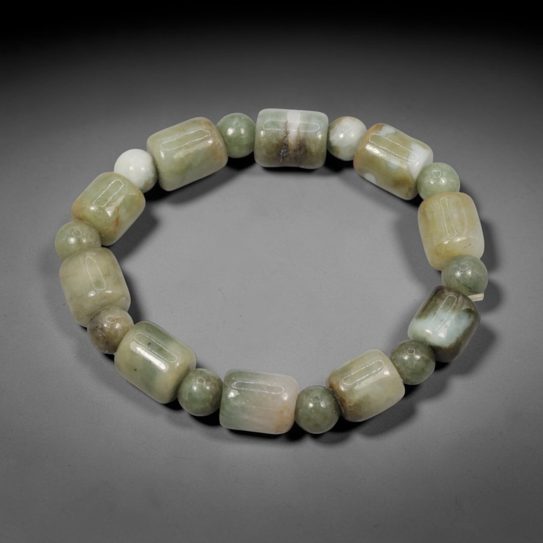 A Chinese Jadeite Jade Bead Bracelet, 20th Century, 31ZK: Composed of a single strand of barrel-shaped and spherical jadeite jade beads forming a circular bracelet. The barrel-shaped beads display natural tonal variation from pale green to deep green, with v