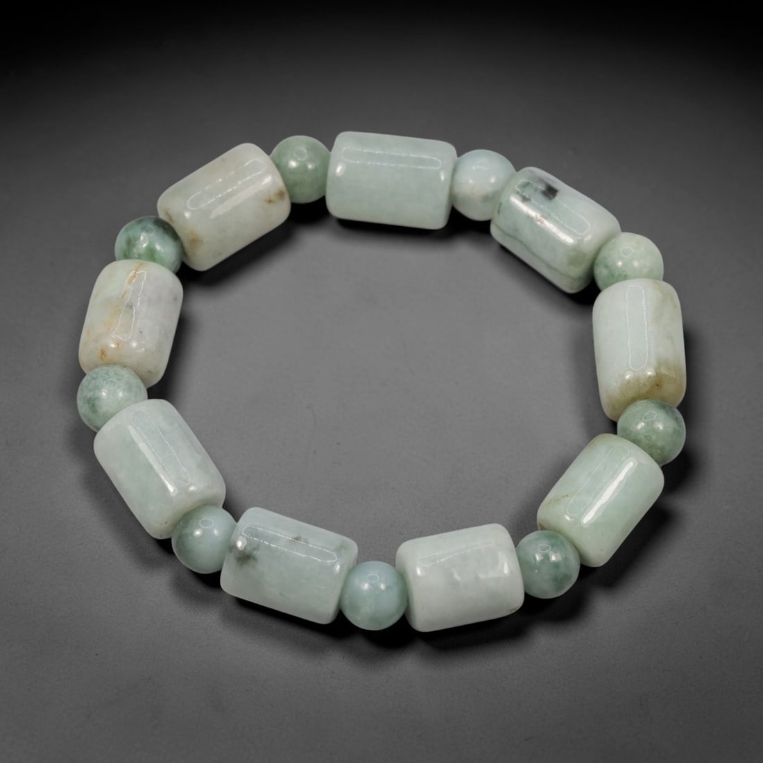 A Chinese Jadeite Jade Bead Bracelet, 20th Century, 35ZK: Composed of a single strand of barrel-shaped and spherical jadeite jade beads forming a circular bracelet. The barrel-shaped beads display natural tonal variation from pale green to light green, with 