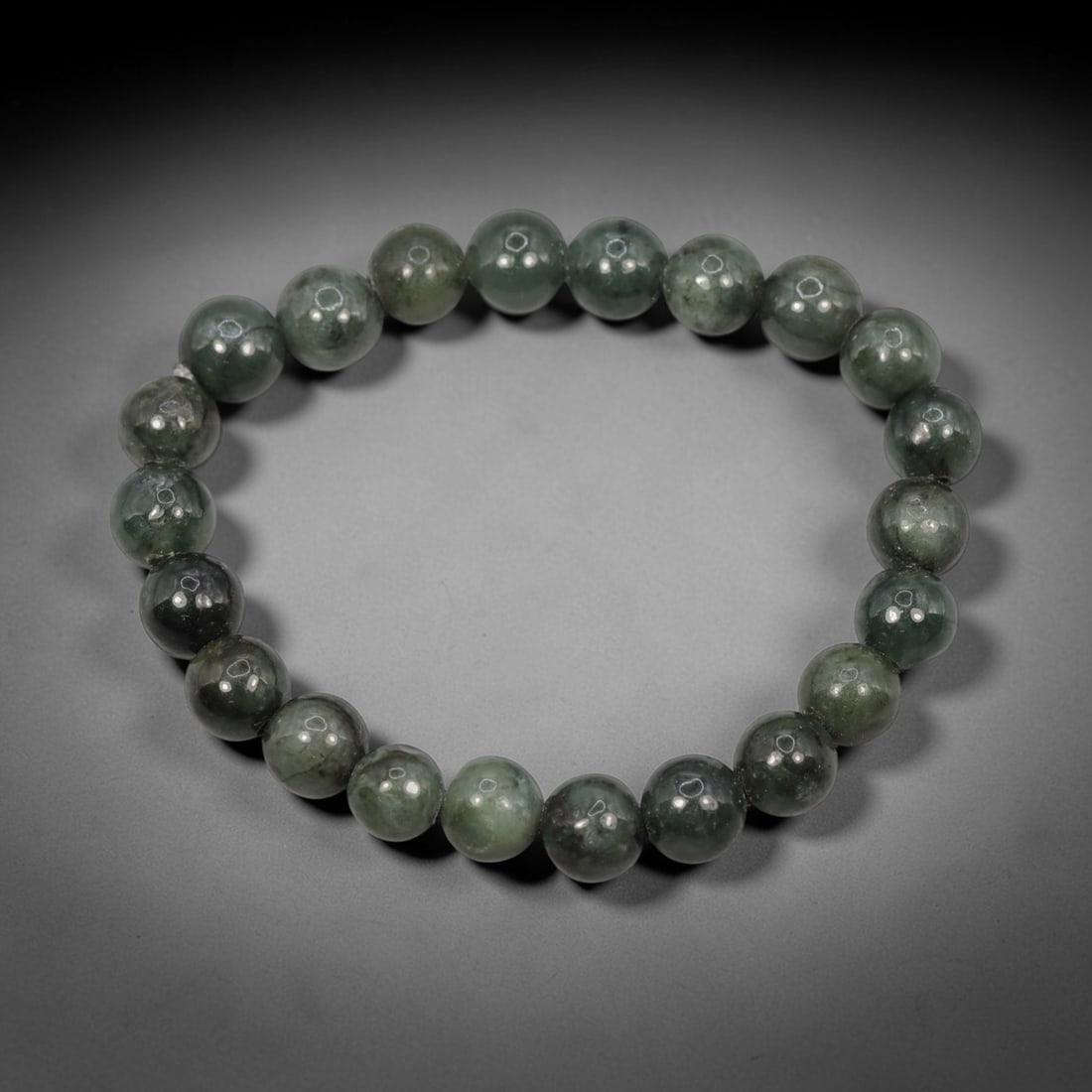 A Chinese Jadeite Jade Bead Bracelet, 20th Century, 57ZK: Composed of a single strand of spherical jadeite jade beads forming a circular bracelet. The beads display natural tonal variation from pale green to deep green, with visible internal mineral inclusio