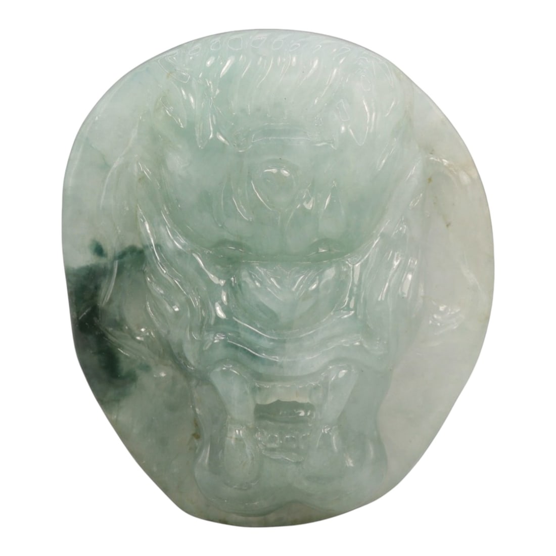 A Chinese Jadeite Jade Dragon Head Pendant, 20th Century, 15ZL: Carved from pale celadon jadeite with natural dark green dendritic inclusions concentrated on the left side, the object is shaped as a flattened, irregular oval. The front is rendered in mid-relief wi