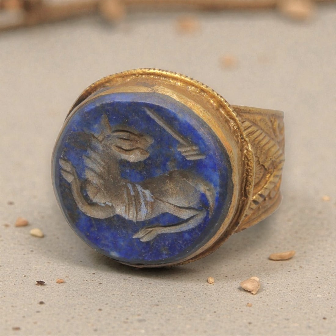 Antique Qajar Dynasty Gilt Intaglio Ring, US Size 7, 36WS: This ring features a circular lapis lazuli intaglio carved with a recumbent quadruped, likely a gazelle, executed in the glyptic style characteristic of Qajar period Iran. The rich blue lapis displays