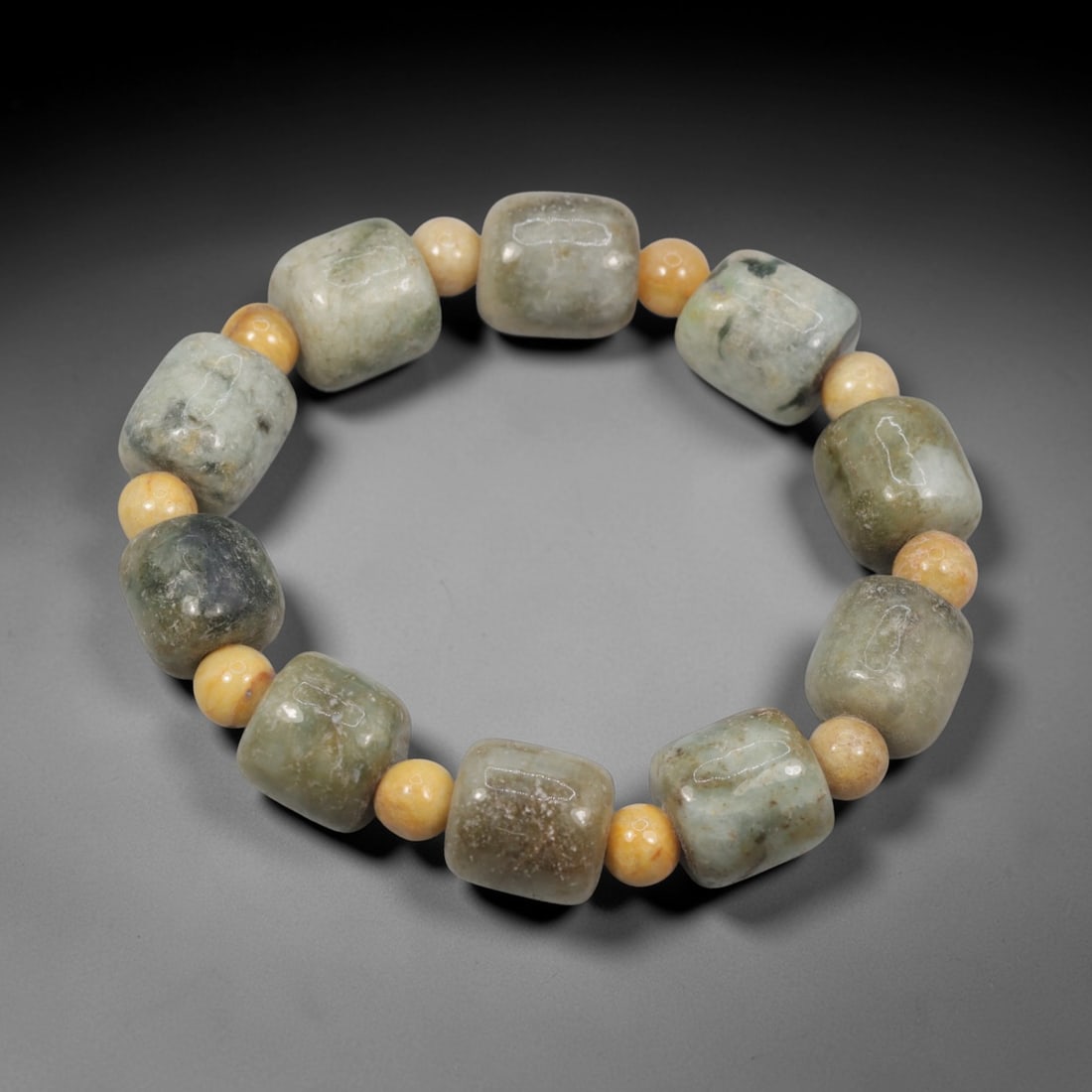 A Chinese Jadeite Jade Bead Bracelet, 20th Century, 38ZK: Composed of a single strand of cuboid and spherical jadeite jade beads forming a circular bracelet. The cuboid beads display natural tonal variation from pale green to deep green, with visible interna