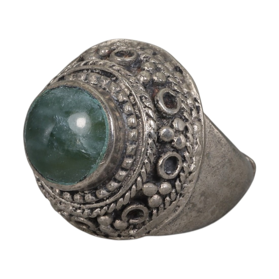 A Middle Eastern Silver Plated Green Agate Ring, Late 19th-Early 20th Century, 17AK: Set with a round cabochon green agate stone exhibiting natural mottled green tones, the ring features an ornate domed bezel decorated with beaded granulation, twisted wirework, and empty circular sett