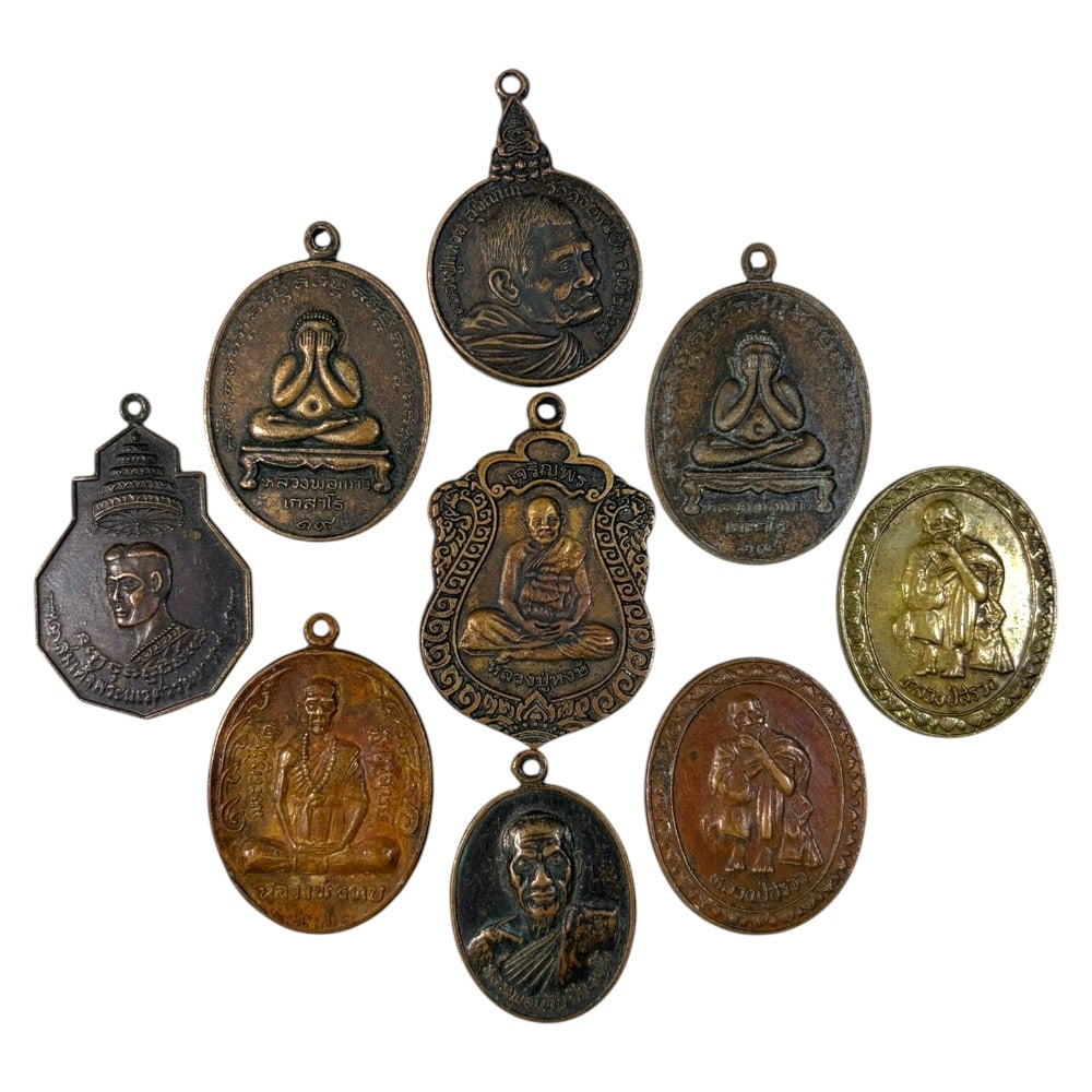 A Lot of 9 Vintage Thai Copper and Bronze Amulets, 47AA: Comprising 9 unmounted pendants ranging from 3 to 4.5 cm in height. The collection features a diverse array of cast metal amulets, including revered monastic portraits, iconic Phra Pidta (closed-eye B
