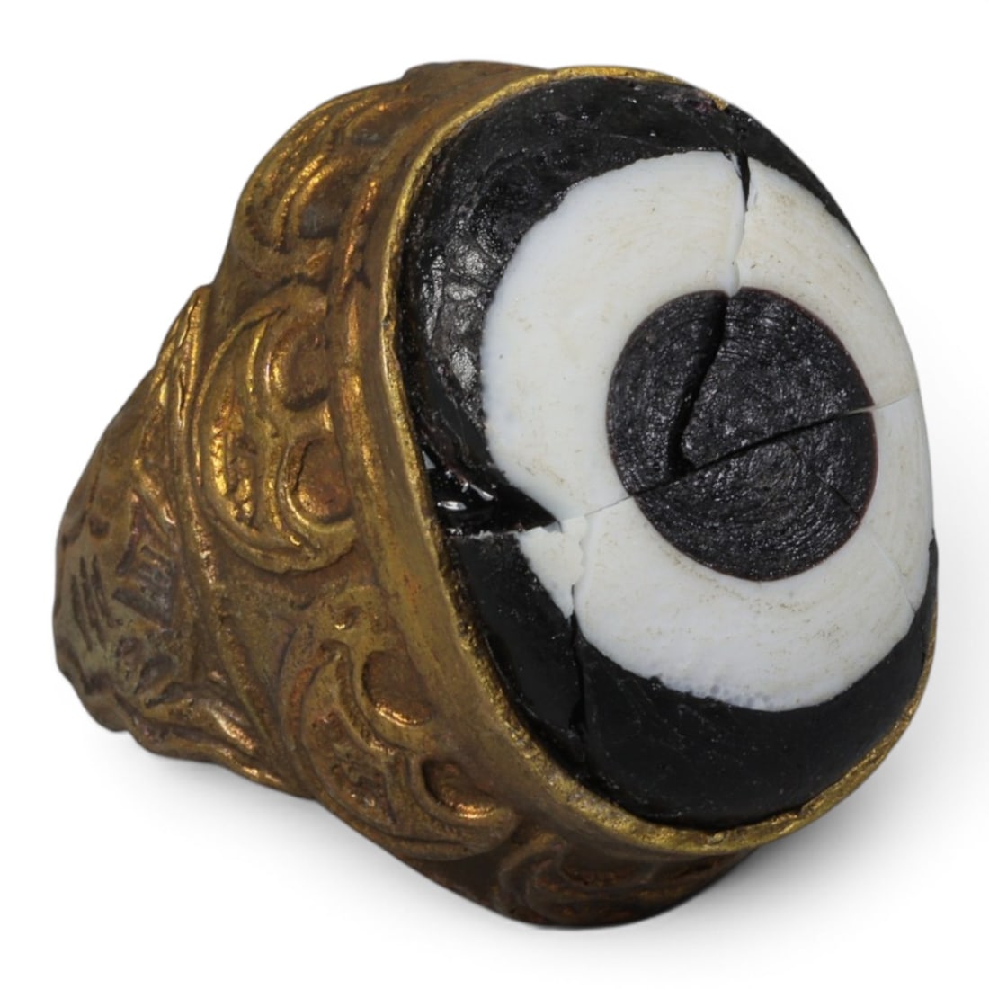 Antique Qajar Dynasty Gilt Evil Eye Ring, US Size 7, 31AJ: A gilt-metal ring of the Qajar period, US ring size 7, featuring a large domed evil-eye glass inlay with a bold concentric black-and-white design (the glass exhibits age-related cracks). The bezel and