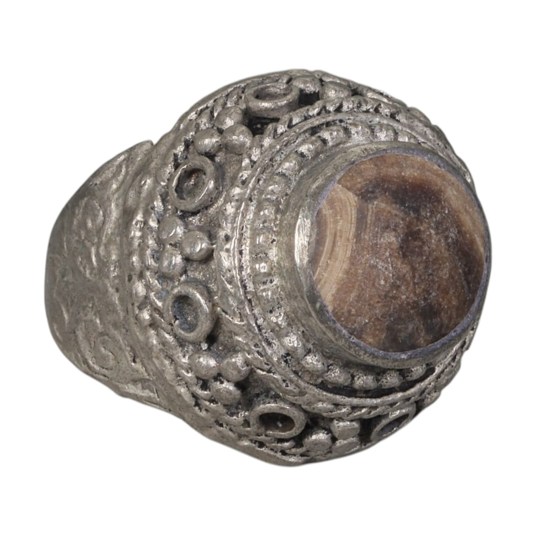 A Middle Eastern Silver Plated Banded Agate Ring, Late 19th-Early 20th Century, 30AK: Set with a round cabochon banded agate stone exhibiting natural layered brown and beige striations, the ring features an ornate domed bezel decorated with beaded granulation, twisted wirework, and emp