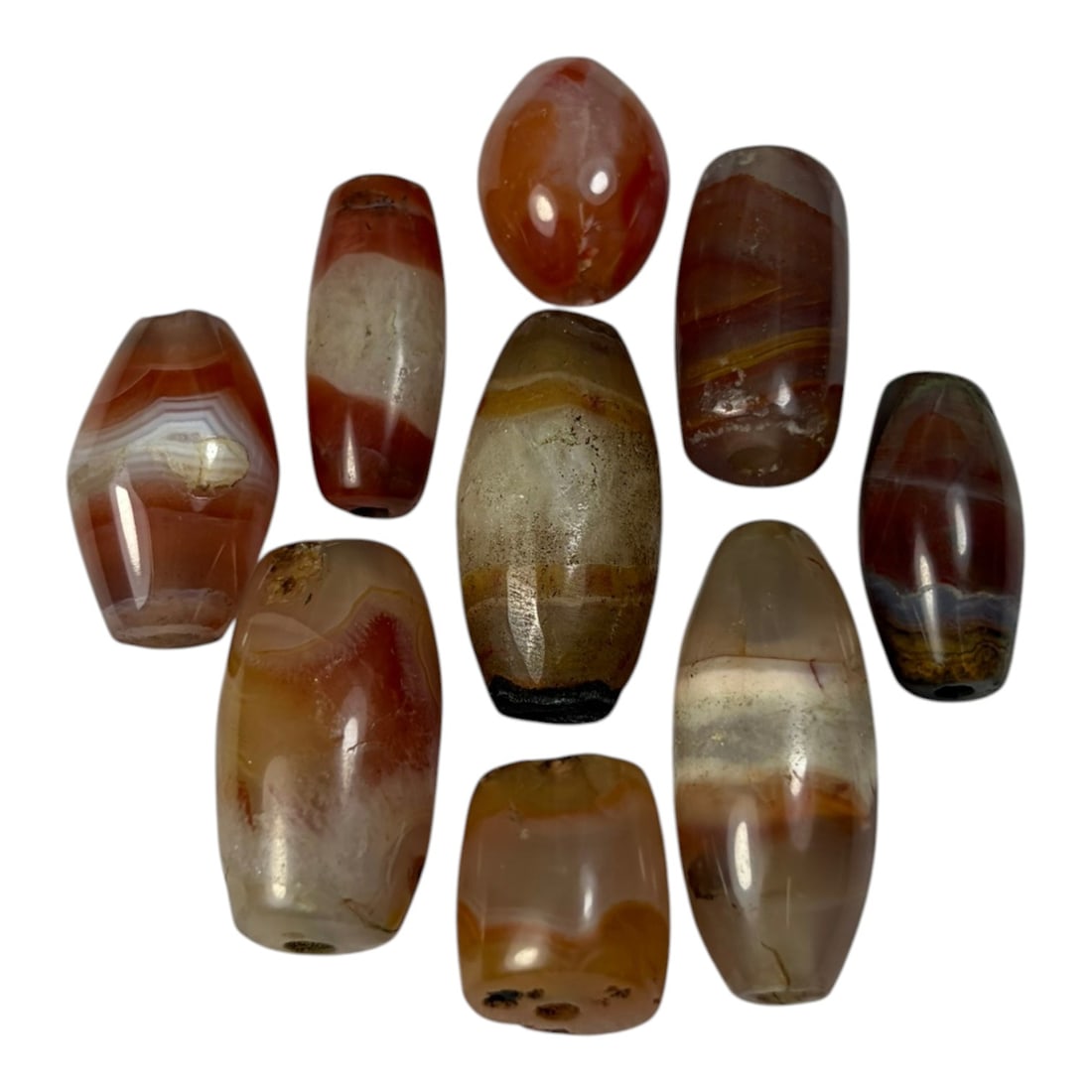 A Lot of 9 Himalayan Banded Agate Beads, Ancient to Antique Period, 44AN: Comprising lot of barrel and ovoid beads, each carved from banded agate with natural tonal variations, many displaying characteristic concentric, linear, and dendritic patterns. The surfaces exhibit s