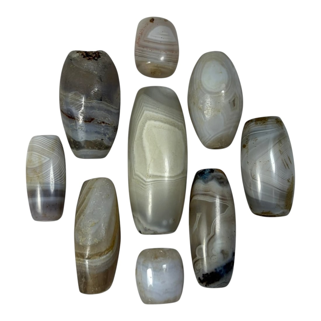 A Lot of 9 Himalayan Banded Agate Beads, Ancient to Antique Period, 38AN: Comprising lot of barrel and ovoid beads, each carved from banded agate with natural tonal variations, many displaying characteristic concentric, linear, and dendritic patterns. The surfaces exhibit s