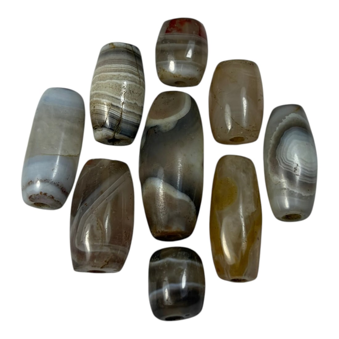 A Lot of 9 Himalayan Banded Agate Beads, Ancient to Antique Period, 43AN: Comprising lot of barrel and ovoid beads, each carved from banded agate with natural tonal variations, many displaying characteristic concentric, linear, and dendritic patterns. The surfaces exhibit s