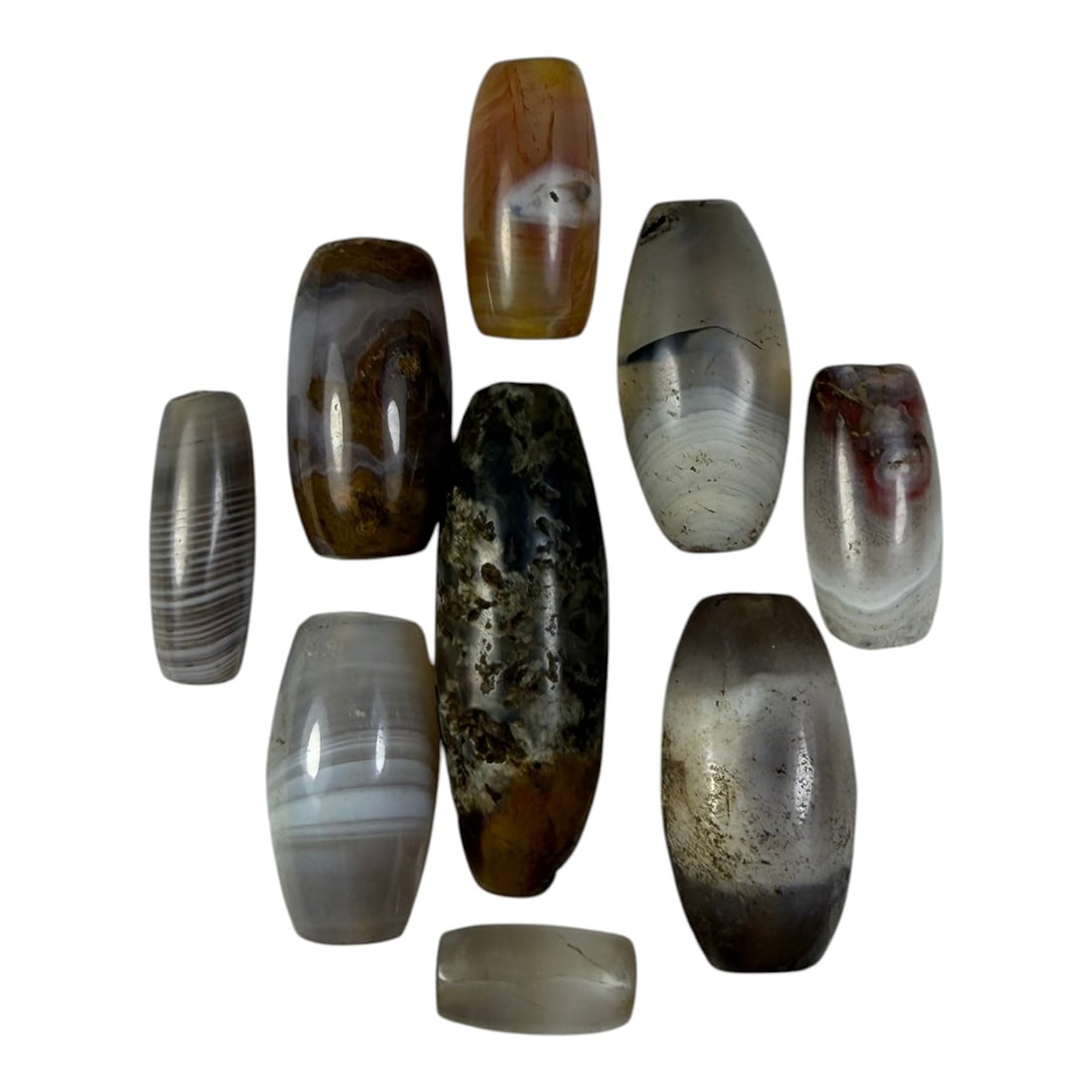 A Lot of 9 Himalayan Banded Agate Beads, Ancient to Antique Period, 17YD: Comprising lot of barrel and ovoid beads, each carved from banded agate with natural tonal variations, many displaying characteristic concentric, linear, and dendritic patterns. The surfaces exhibit s