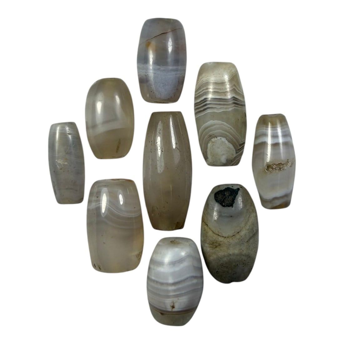 A Lot of 9 Himalayan Banded Agate Beads, Ancient to Antique Period, 28YD: Comprising lot of barrel and ovoid beads, each carved from banded agate with natural tonal variations, many displaying characteristic concentric, linear, and dendritic patterns. The surfaces exhibit s