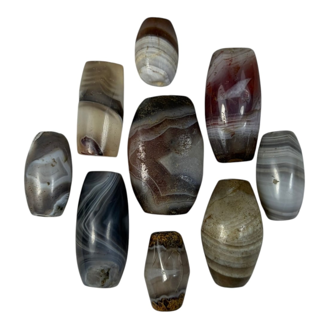 A Lot of 9 Himalayan Banded Agate Beads, Ancient to Antique Period, 20YD: Comprising lot of barrel and ovoid beads, each carved from banded agate with natural tonal variations, many displaying characteristic concentric, linear, and dendritic patterns. The surfaces exhibit s