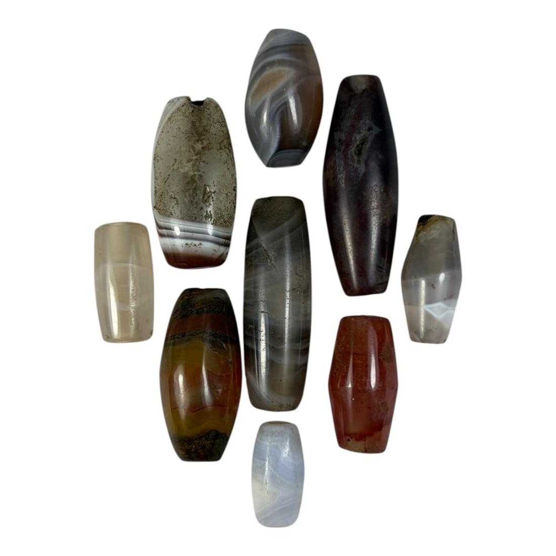 A Lot of 9 Himalayan Banded Agate Beads, Ancient to Antique Period, 18YD: Comprising lot of barrel and ovoid beads, each carved from banded agate with natural tonal variations, many displaying characteristic concentric, linear, and dendritic patterns. The surfaces exhibit s