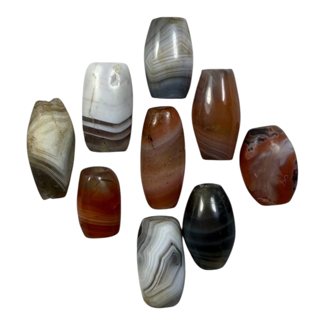 A Lot of 9 Himalayan Banded Agate Beads, Ancient to Antique Period, 34YD: Comprising lot of barrel and ovoid beads, each carved from banded agate with natural tonal variations, many displaying characteristic concentric, linear, and dendritic patterns. The surfaces exhibit s