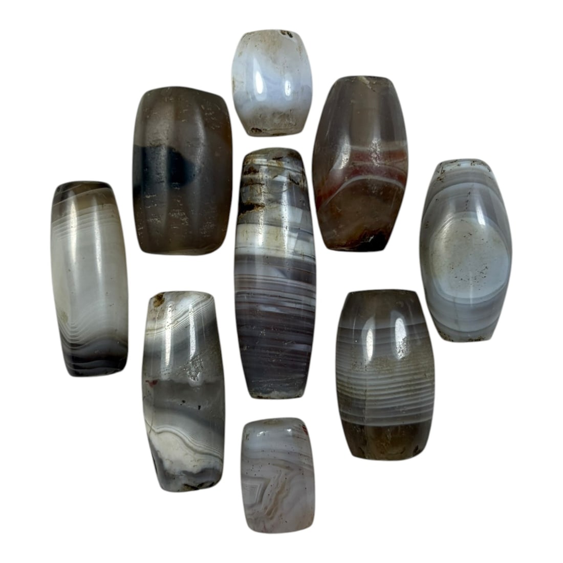 A Lot of 9 Himalayan Banded Agate Beads, Ancient to Antique Period, 32YD: Comprising lot of barrel and ovoid beads, each carved from banded agate with natural tonal variations, many displaying characteristic concentric, linear, and dendritic patterns. The surfaces exhibit s