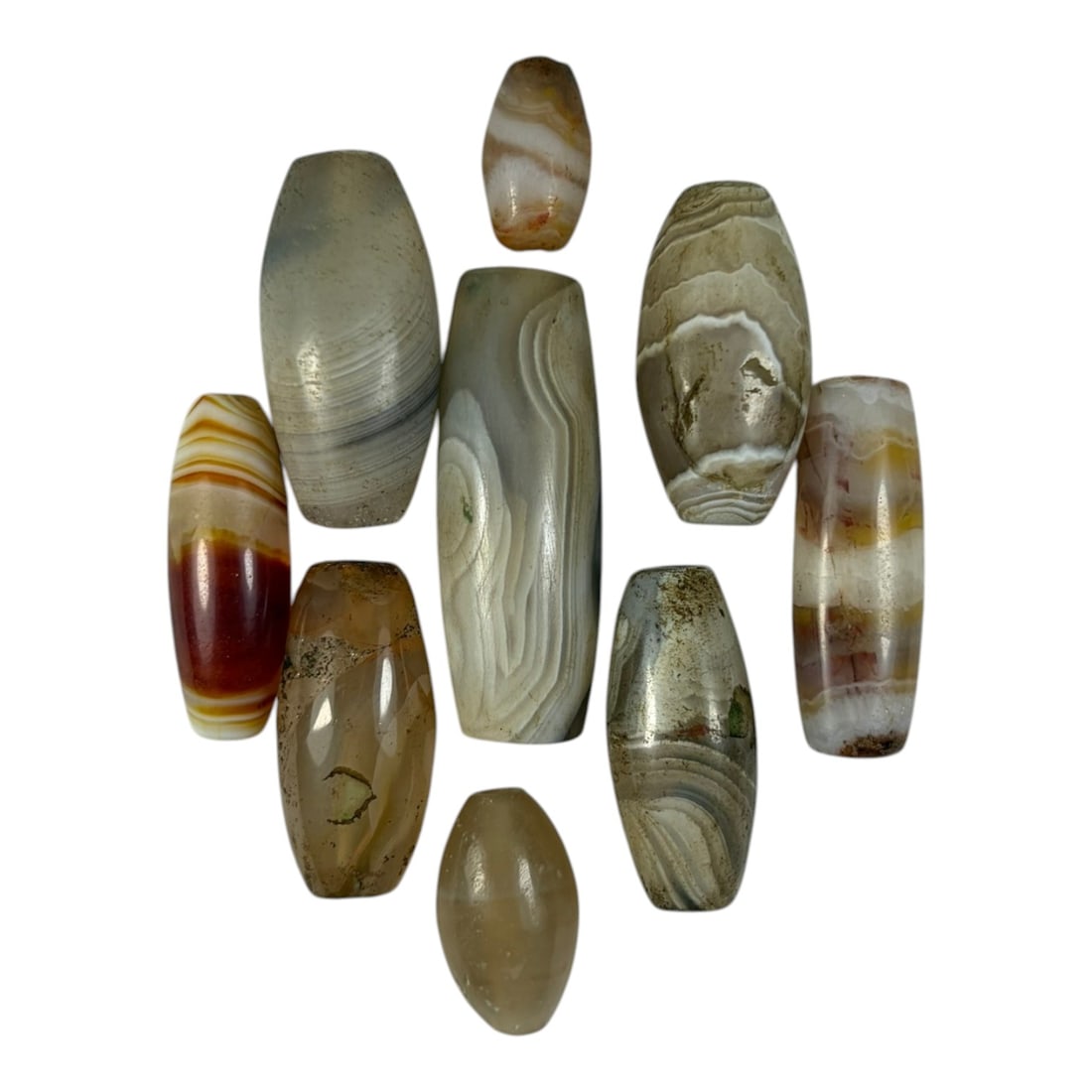 A Lot of 9 Himalayan Banded Agate Beads, Ancient to Antique Period, 25YD: Comprising lot of barrel and ovoid beads, each carved from banded agate with natural tonal variations, many displaying characteristic concentric, linear, and dendritic patterns. The surfaces exhibit s