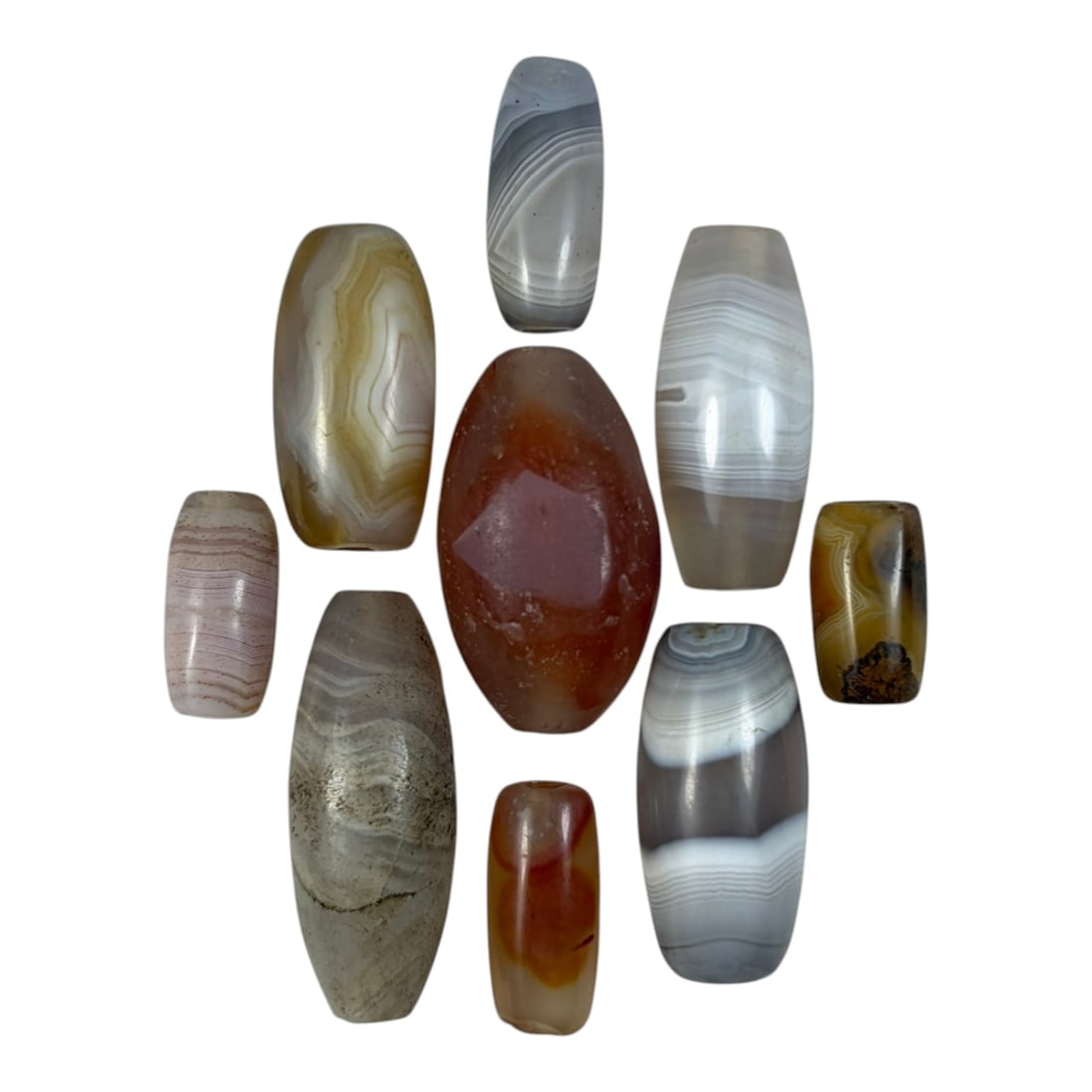 A Lot of 9 Himalayan Banded Agate Beads, Ancient to Antique Period, 22YD: Comprising lot of barrel and ovoid beads, each carved from banded agate with natural tonal variations, many displaying characteristic concentric, linear, and dendritic patterns. The surfaces exhibit s
