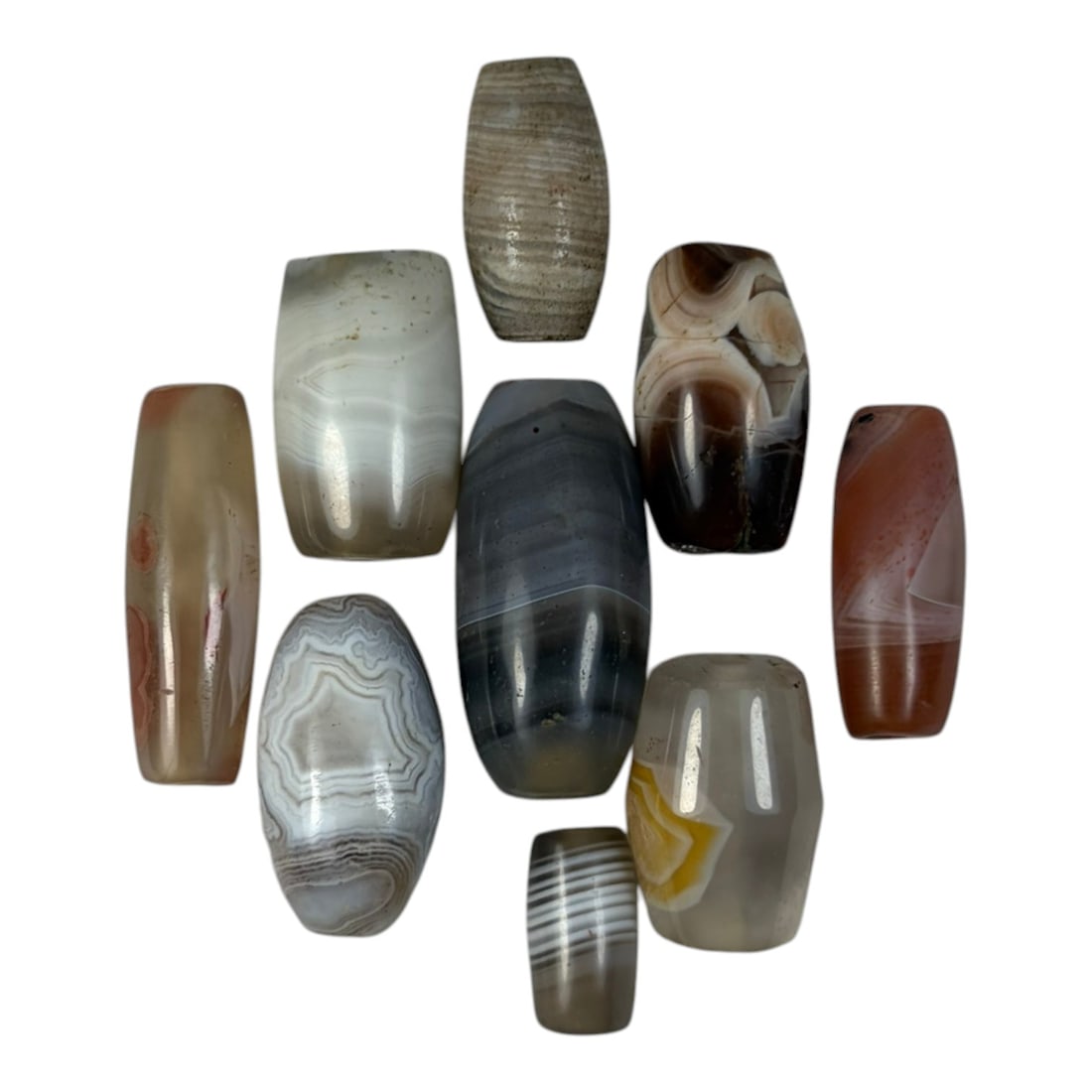 A Lot of 9 Himalayan Banded Agate Beads, Ancient to Antique Period, 31YD: Comprising lot of barrel and ovoid beads, each carved from banded agate with natural tonal variations, many displaying characteristic concentric, linear, and dendritic patterns. The surfaces exhibit s