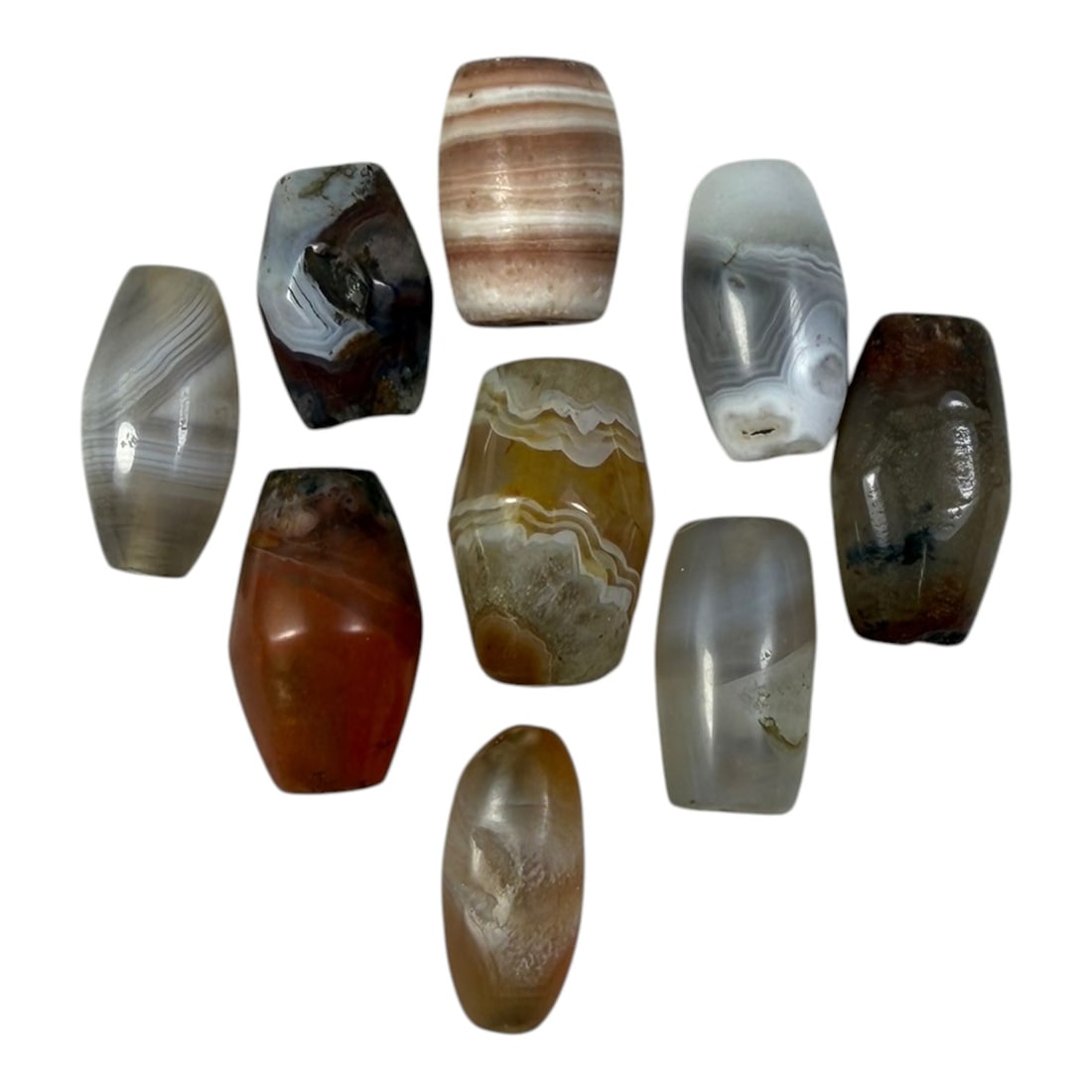 A Lot of 9 Himalayan Banded Agate Beads, Ancient to Antique Period, 15YD: Comprising lot of barrel and ovoid beads, each carved from banded agate with natural tonal variations, many displaying characteristic concentric, linear, and dendritic patterns. The surfaces exhibit s