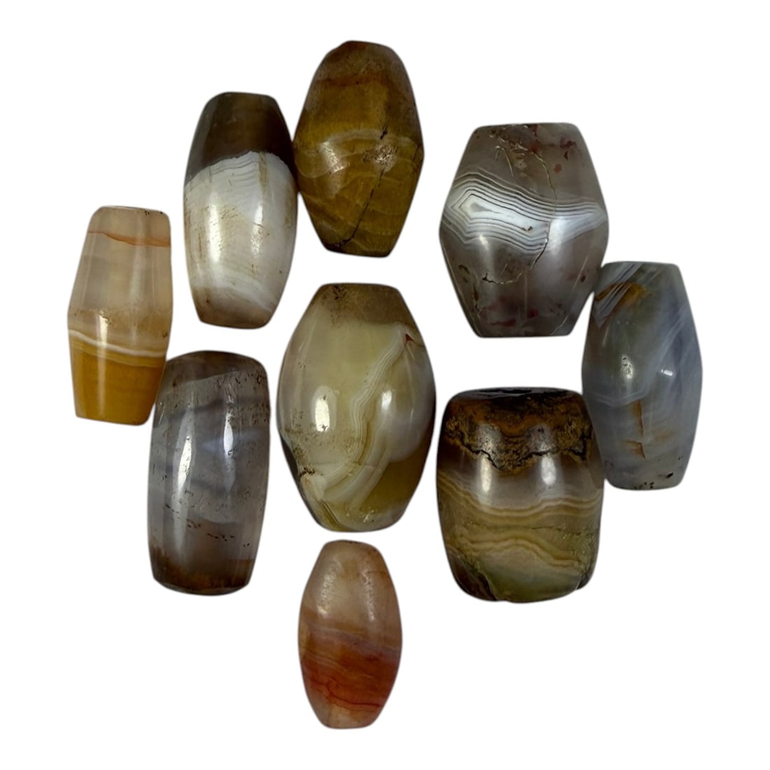 A Lot of 9 Himalayan Banded Agate Beads, Ancient to Antique Period, 16YD: Comprising lot of barrel and ovoid beads, each carved from banded agate with natural tonal variations, many displaying characteristic concentric, linear, and dendritic patterns. The surfaces exhibit s