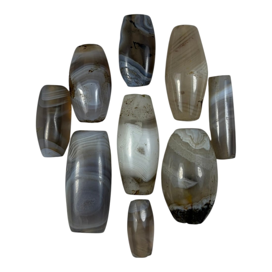 A Lot of 9 Himalayan Banded Agate Beads, Ancient to Antique Period, 23YD: Comprising lot of barrel and ovoid beads, each carved from banded agate with natural tonal variations, many displaying characteristic concentric, linear, and dendritic patterns. The surfaces exhibit s