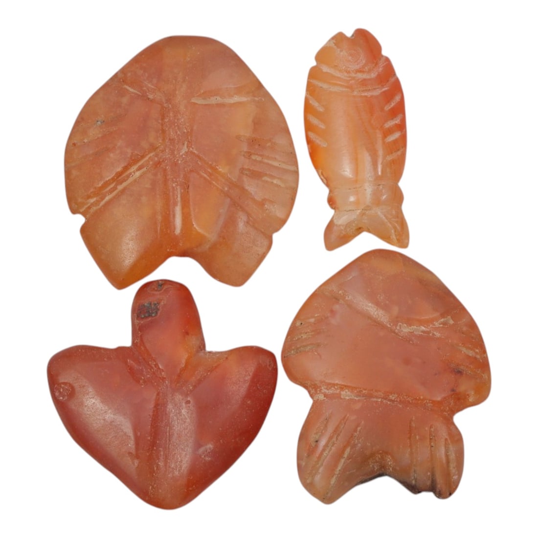 Lot of 4 Coptic Egyptian Carnelian Amulets, Circa Roman to Coptic Era, 17WS: The group consists of four carnelian amulets, each carved from orange-red stone with natural banding, translucency, and surface patina. The forms include stylized fish and bird/leaf motifs, with incis