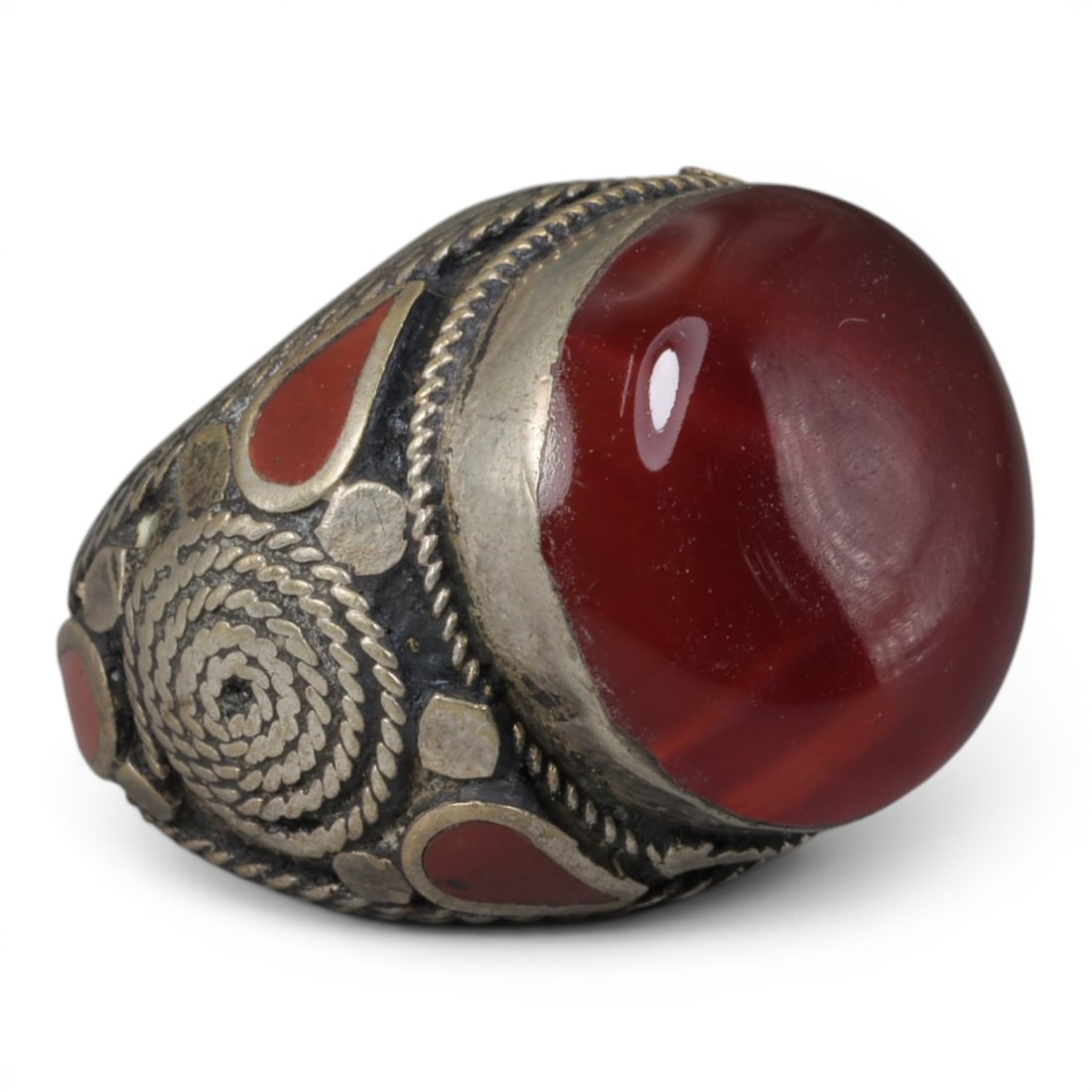 Antique Central Asian Silver and Carnelian Tribal Ring, 19th-Early 20th Century, 68AJ: The ring is set with a large, smooth cabochon carnelian stone, displaying natural banding within its deep red matrix. The silver mount is decorated with pseudo-filigree wirework, a spiral motif, and i