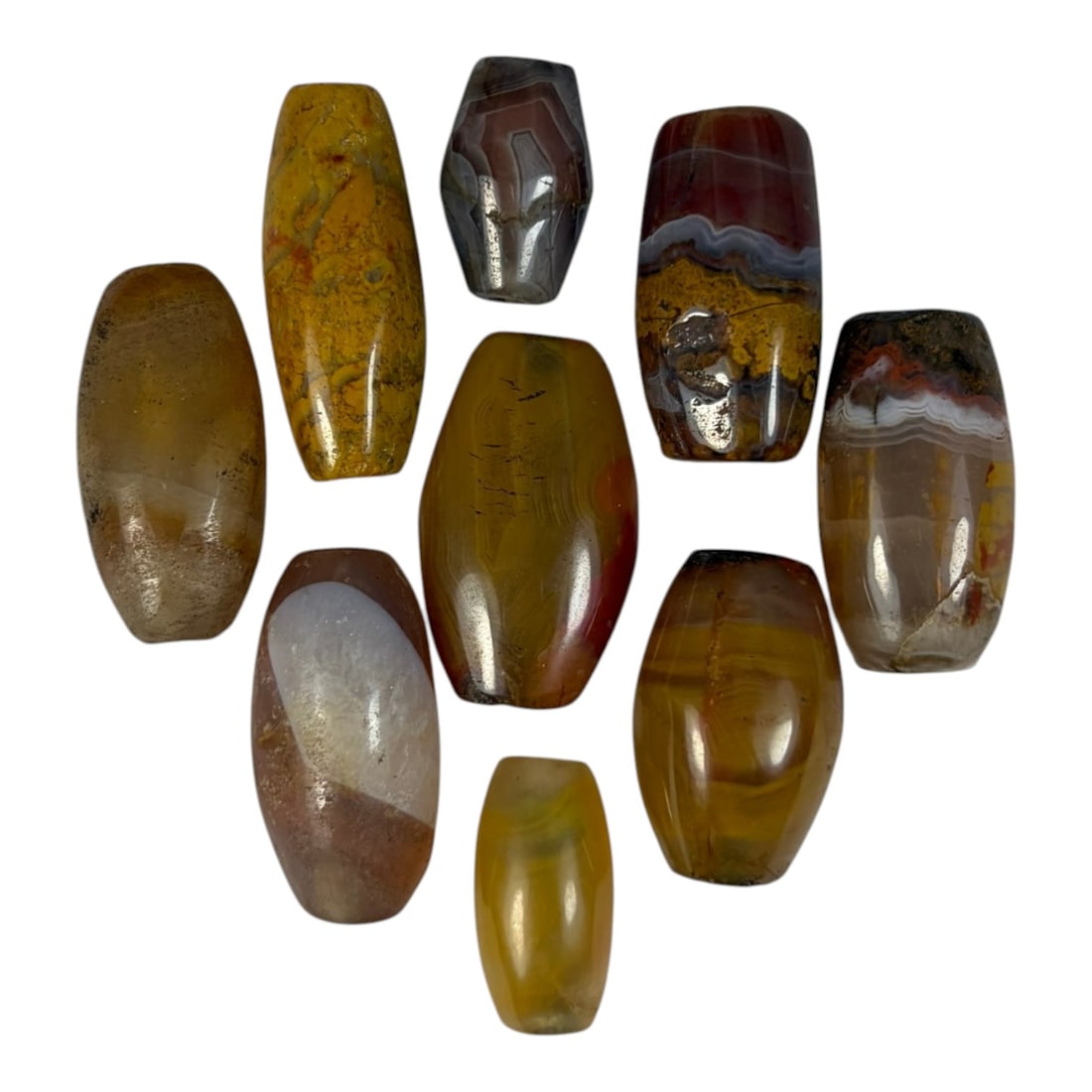 A Lot of 9 Himalayan Banded Agate Beads, Ancient to Antique Period, 27YD: Comprising lot of barrel and ovoid beads, each carved from banded agate with natural tonal variations, many displaying characteristic concentric, linear, and dendritic patterns. The surfaces exhibit s