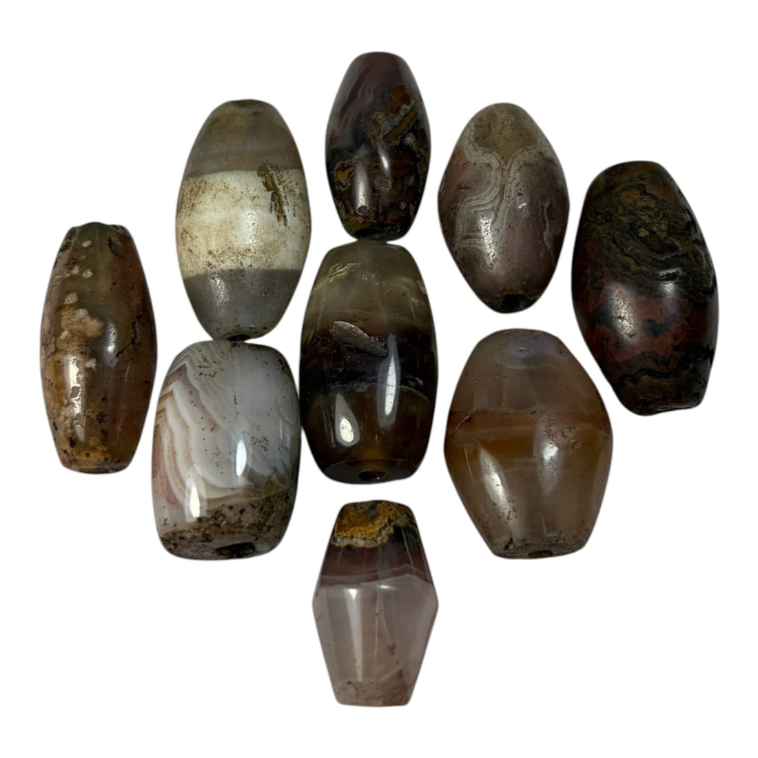 A Lot of 9 Himalayan Banded Agate Beads, Ancient to Antique Period, 48AN: Comprising lot of barrel and ovoid beads, each carved from banded agate with natural tonal variations, many displaying characteristic concentric, linear, and dendritic patterns. The surfaces exhibit s