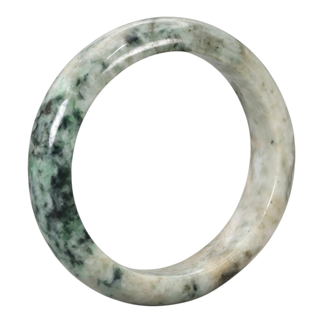 A Chinese Jadeite Jade Bangle Bracelet, 20th Century, 84ZK: Carved from jadeite jade with a pale off-white base and irregular dark green mottled inclusions, the bangle is shaped as a solid, continuous circular band with a classic rounded cross-section. The sur