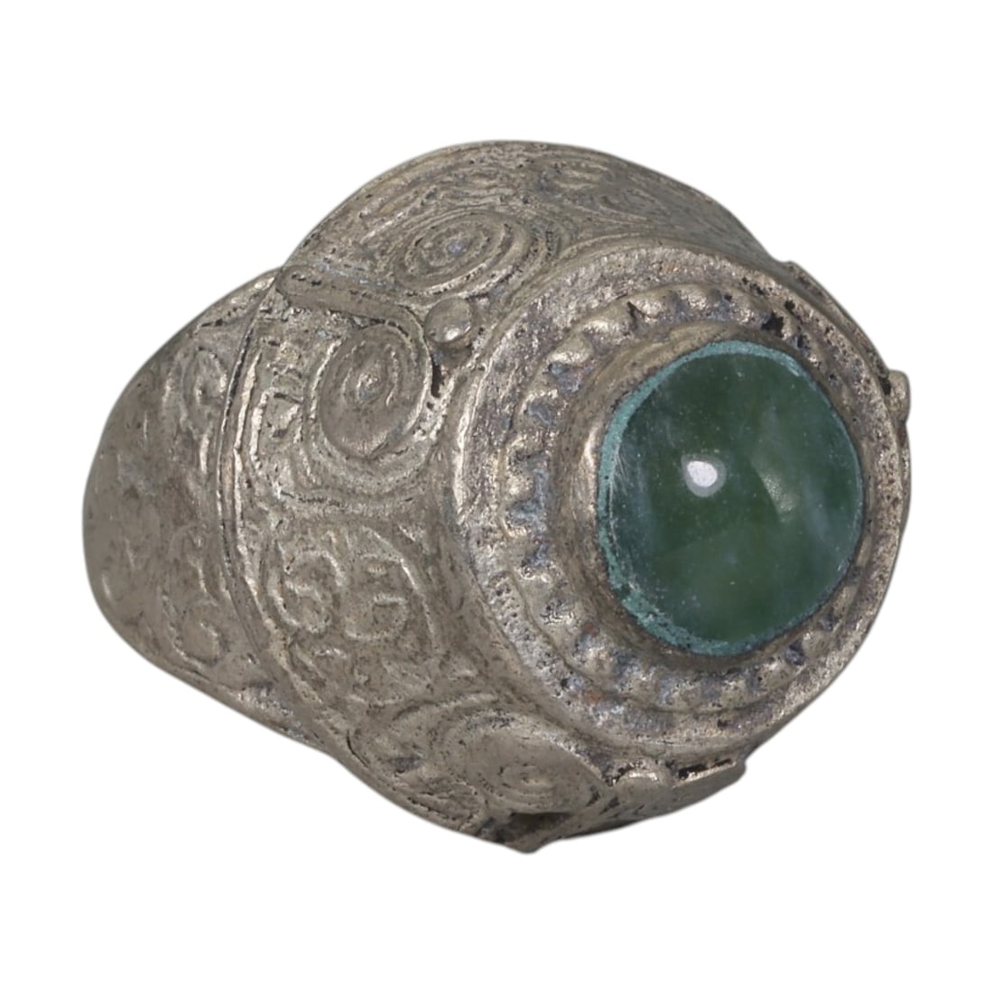 A Middle Eastern Silver Plated Green Agate Ring, Late 19th-Early 20th Century, 18AK: The ring is centered with a round cabochon green agate stone set within a domed bezel featuring a raised beaded border. The bezel and shoulders are engraved with stylized spiral and foliate motifs. Th
