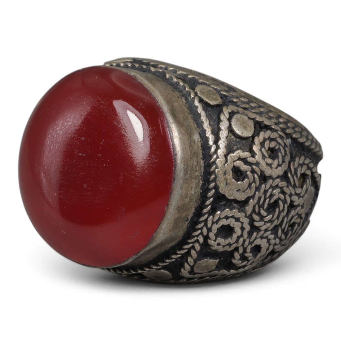 Antique Central Asian Silver and Carnelian Tribal Ring, 19th-Early 20th Century, 61AJ: The ring is set with a large, smooth cabochon carnelian stone. The silver mount is decorated with pseudo-filigree wirework and applied coiled motifs, set against a darkened background. The metal exhib