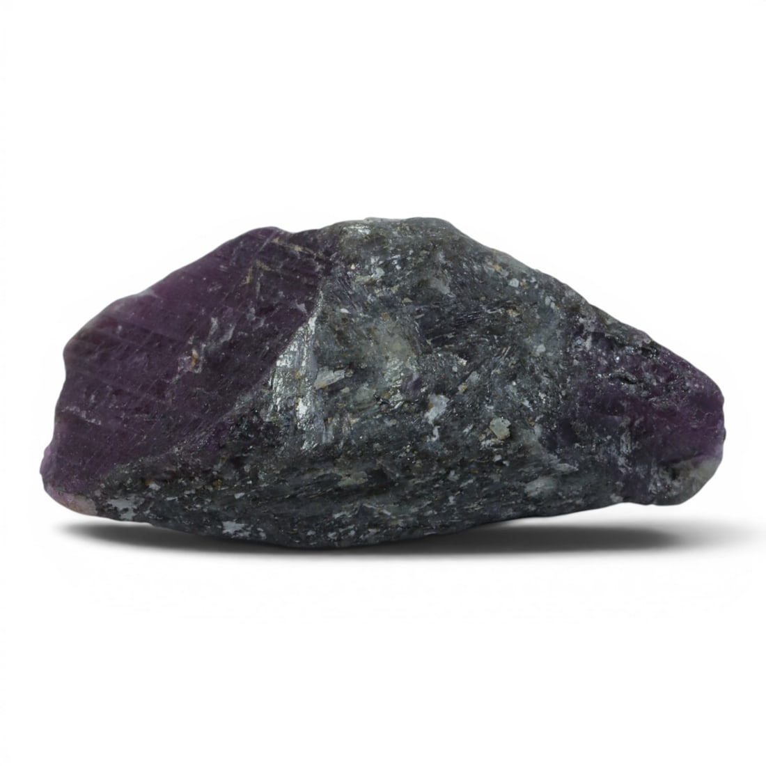 25.10ct Natural Mauritania Ruby Rough (Unheated), 71XA: This unheated Mauritania ruby rough is a captivating natural crystal specimen, showcasing a vivid, saturated magenta-purple ruby section embedded in a rugged dark grey matrix. The exposed ruby face re