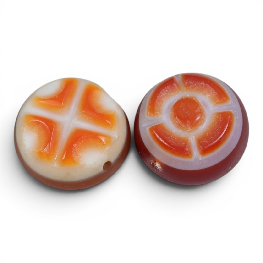A Pair of Antique Himalayan Banded Carnelian Beads, 75AJ: The pair consists of two round, flat carnelian beads, each showcasing unique natural banding patterns. The left bead features a four-lobed cross motif in orange against a creamy white background, whil
